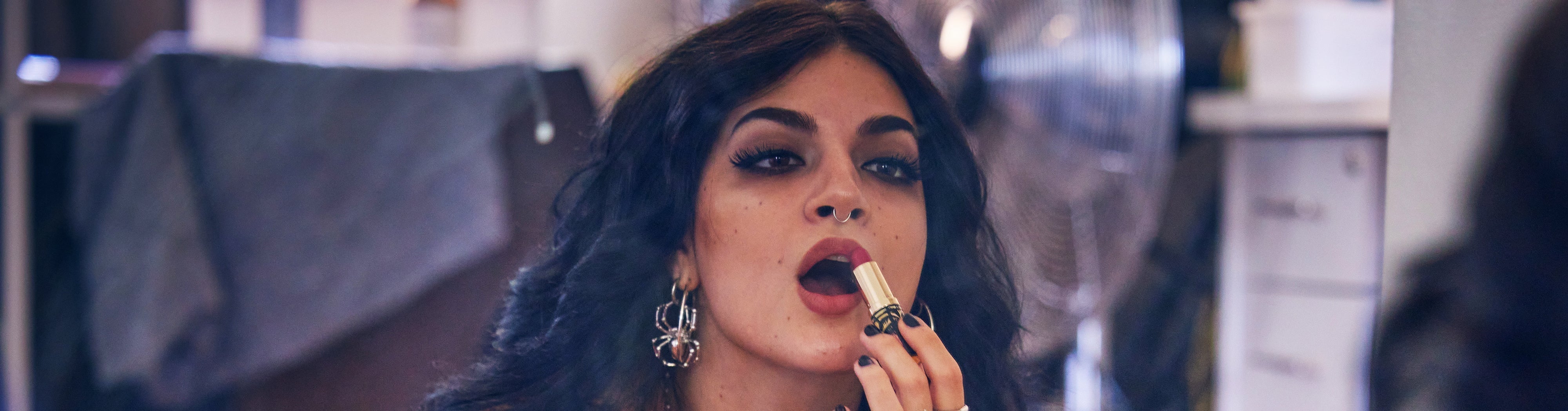 Woman applying Peep lipstick in a mirror, showcasing makeup artistry in a vibrant beauty environment.